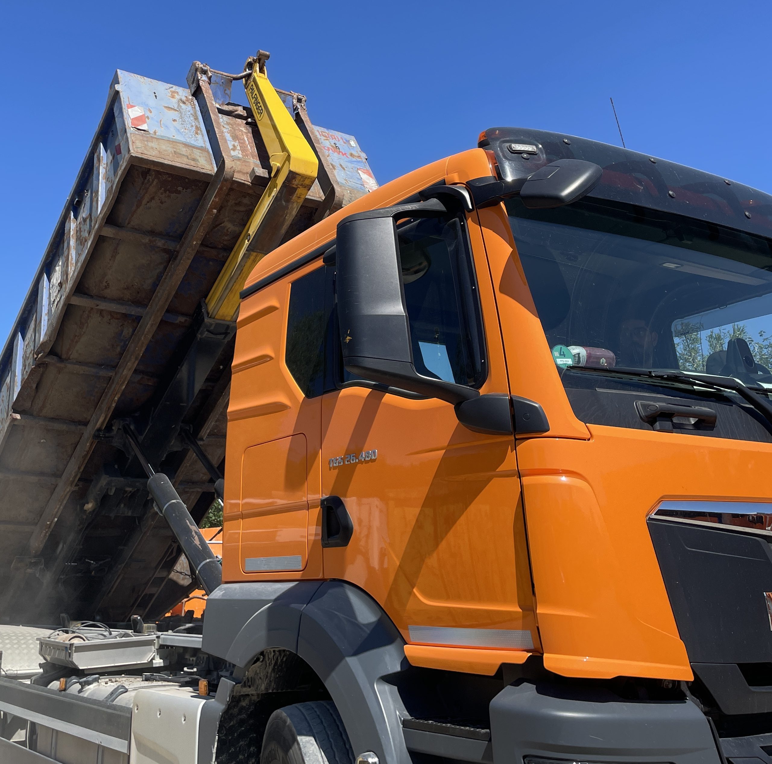 Oranger MAN LKW kippt Container vor blauem Himmel